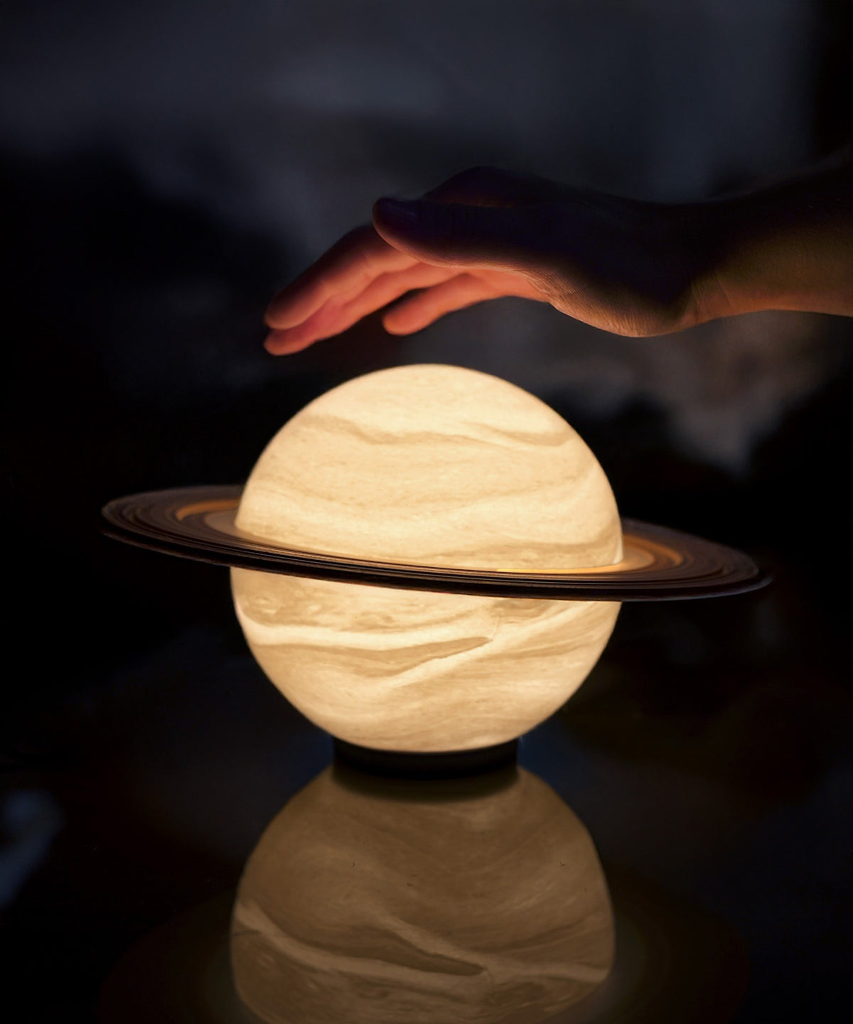 Saturn Planet Lamp — lit on its black base on a dark reflective table